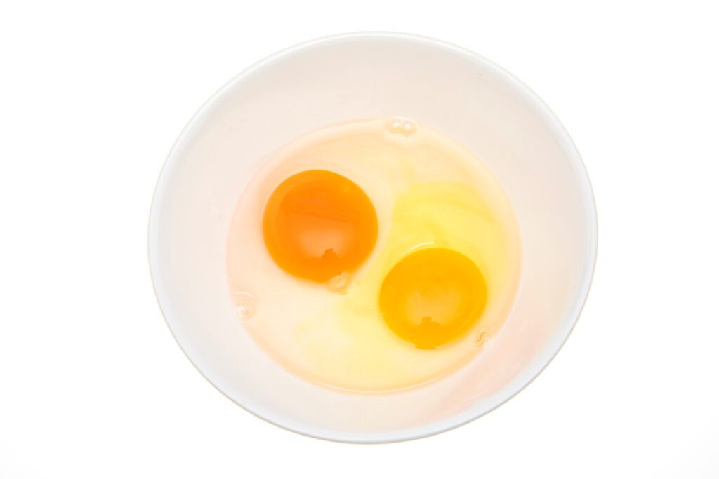 A white bowl with a duck egg yolk and white on one side and a chicken egg yolk and white on the other.